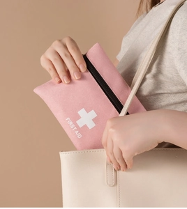 Pink portable first aid pouch with white cross logo being placed into a beige tote bag