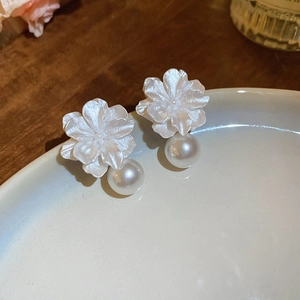 Close-up of white resin flower earrings with elegant pearls and silver needle studs