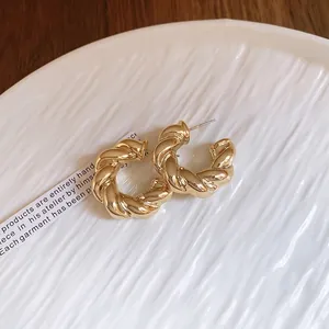 Elegant gold chunky C-shaped twisted hoop earrings on a decorative white ceramic tray