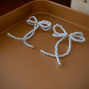 Close-up of elegant pearl bow earrings with gold metal links on a display tray