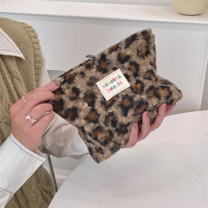 Detail of plush leopard print makeup bag with woven label held by hand in soft lighting