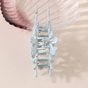 Conch shell hair claw clip in light blue with purple spots on a soft pink background