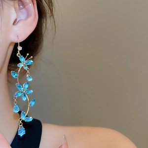 Detailed view of long tassel earrings with blue floral crystals and gold finish on model