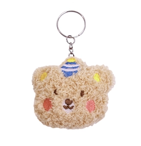 Macro detail of khaki plush bear keychain with embroidery and blue striped horn detail