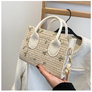 Close-up of beige straw woven handbag featuring elegant flower embroidery and white handle