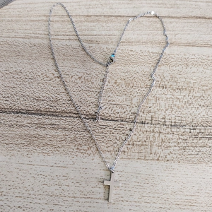 Detailed view of a silver stainless steel cross pendant necklace on a rustic wood background