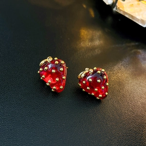 Macro shot of sweet red strawberry earrings with golden leaf details on black leather