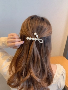 Close-up of elegant golden hair clip with pearls and rhinestones on long brown hair