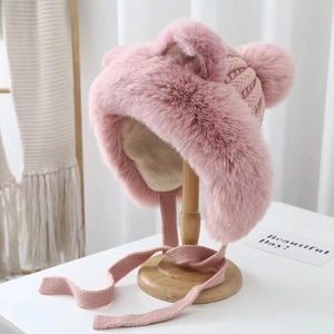 Detail of pink plush faux fur winter hat with cute ears and knit straps on a wooden stand