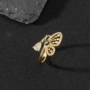 Golden butterfly open ring with zircon and blue evil eye charms on a natural stone surface