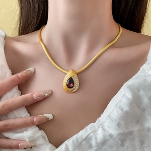 Detailed view of a gold teardrop necklace featuring a deep red gemstone and rhinestones