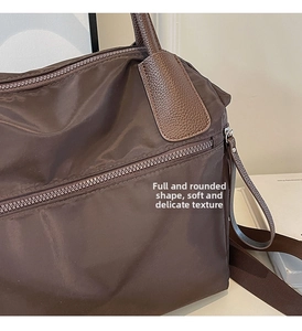 Detail of dark brown nylon bag showing leather zipper pull and woven shoulder strap