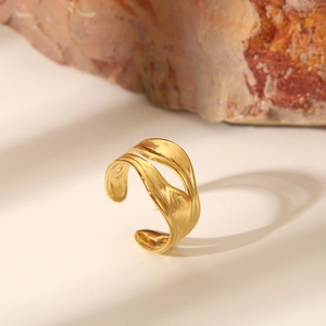 Close-up of golden wavy textured open ring on a minimalist stone background