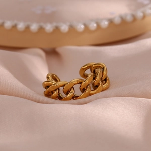 Macro shot of gold Cuban chain link ring on soft pink silk fabric with pearl details