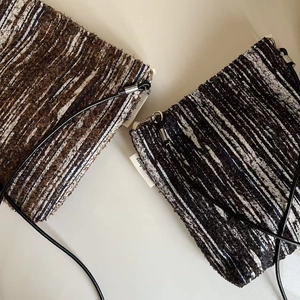 Detail view of striped woven crossbody bags in brown and navy blue with leather straps