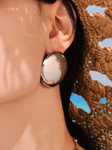 Polished silver heart-shaped stud earrings shown on a model in a summer vacation setting