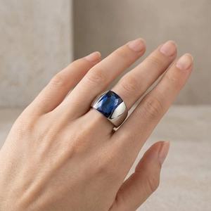 Detail of wide stainless steel ring with rectangular blue gemstone on model hand