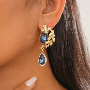 Detailed view of luxury dark blue gemstone earrings in a gold setting on model