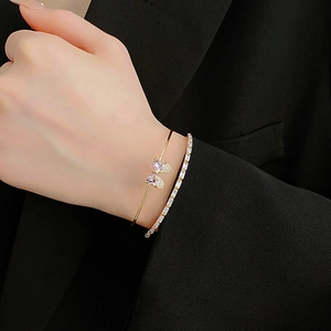 Detail view of a gold bow cuff bracelet with zircon and a matching tennis bracelet on wrist