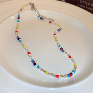 Detail of colorful beaded choker with silver cubes and lobster clasp on white ceramic