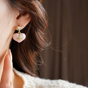 Close-up of heart-shaped drop earring with pink enamel and gold plating on model
