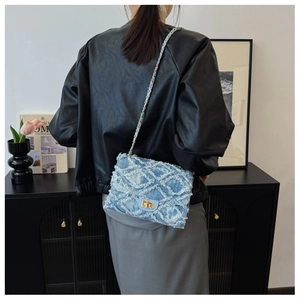 Détail du sac à rabat en denim bleu clair avec texture matelassée et chaîne dorée