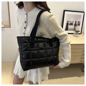 Detail shot of a black quilted puffer tote bag featuring square stitching and wide straps