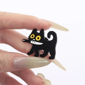 Close-up of a cute black and yellow enamel cat brooch held in hand over a white background