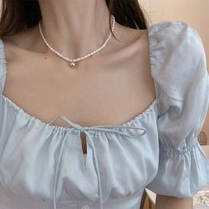 Detailed view of natural pearl necklace featuring a gold heart pendant on a female model