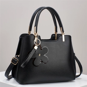 Detail of black lychee grain leather tote with gold hardware and floral pendant