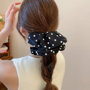 Detail view of a black polka dot scrunchie with pearl lace trim worn on a high ponytail