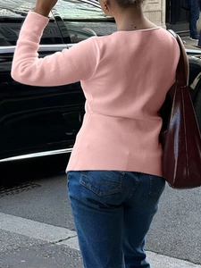 Back view of a pink long-sleeved knitted top paired with blue jeans in a street setting
