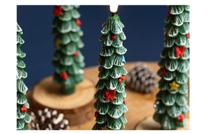 Detailed view of green Christmas tree candle with snow effect and red bow ornament