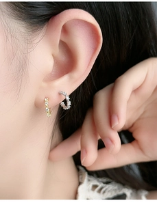 Close-up detail of silver and gold paved hoop earrings worn on earlobe and cartilage