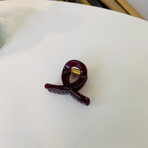 Macro detail of wine red hair claw clip with glossy resin finish and gold spring