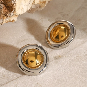 Macro shot of two-tone gold and silver circular stud earrings on a beige stone surface