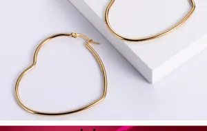 Close-up of oversized golden heart-shaped hoop earrings on white stone display