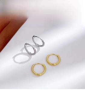 Detail of gold and silver twisted hoop earrings with textured woven pattern on white background