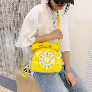 Close-up of bright yellow patent leather retro telephone shaped crossbody bag on a model