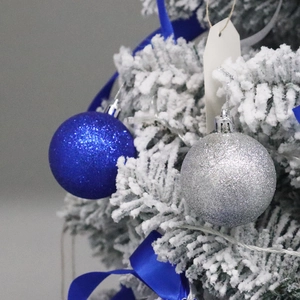 Blue and silver glitter Christmas balls hanging on a snowy tree for festive decoration