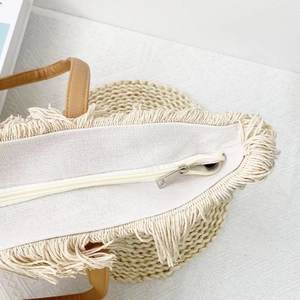 Dettaglio della borsa tote intrecciata beige con cerniera argento e bordi a frange