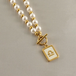 Detail of gold Libra zodiac pendant necklace with white pearls and a toggle clasp