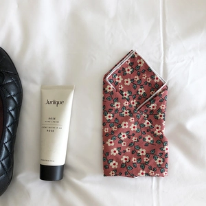 Flat lay of red floral cotton linen scarf beside a 100ml tube of Jurlique rose hand cream