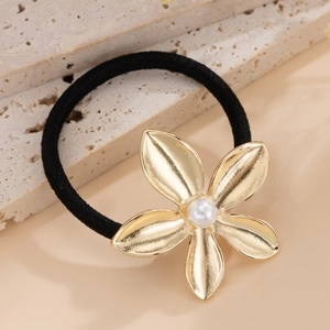 Close-up of golden five-petal flower hair tie with pearl center on marble background