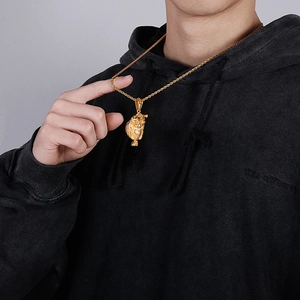 Close-up of a gold owl pendant on a twist chain worn by a model in a black hoodie