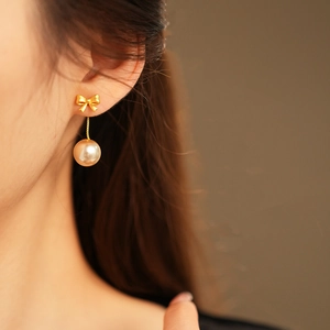 Close-up of elegant gold bow and pearl drop earrings on model for a French vintage look