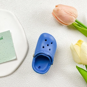 Close-up of bright blue mini slipper phone stand with breathable holes on white texture
