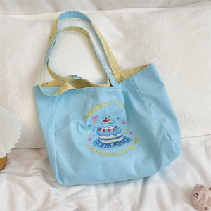 Detail of light blue canvas tote bag featuring cake embroidery and yellow plaid lining