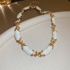 Détail macro du collier en résine blanche avec maillons croisés en X dorés