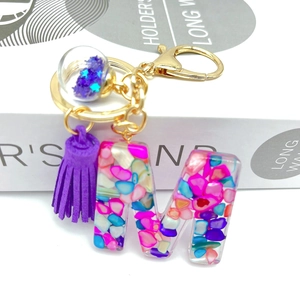 Detail of resin letter M keychain with purple tassel and colorful stones on a gift box